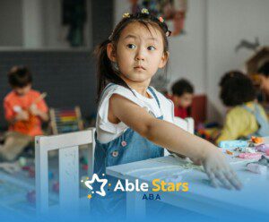 Autistic girl playing with clay at a table during center-based ABA therapy with other children.