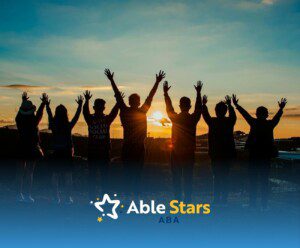 A group of autistic adults raising hands in front of a sunset sky at a hilltop in Maryland.