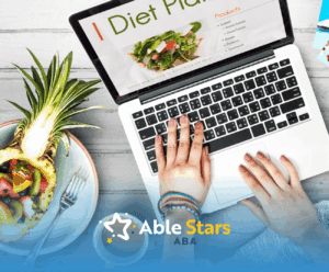 An autistic individual typing an autism diet plan on a laptop with a plate of fruits beside