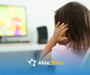 A little girl covering her ears, sitting in front of a computer.