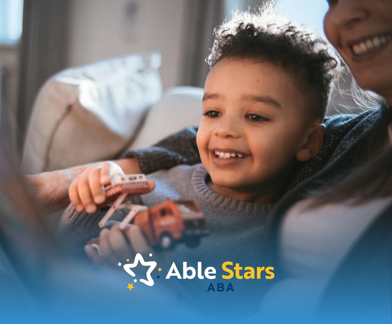 Smiling autistic child playing with toy cars while sitting close to an ABA therapist in Maryland.