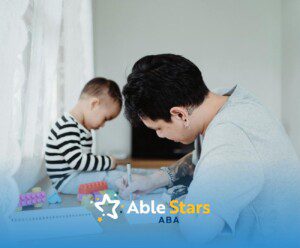 An ABA therapist writing in a notebook while autistic child plays with blocks at home in Maryland.
