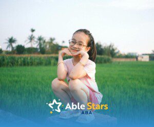 Smiling autistic girl with ADHD in pink squatting outdoors at a lush green field in Maryland.