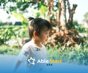 Autistic toddler with short ponytail standing outside in a sunny, green garden area in Maryland.