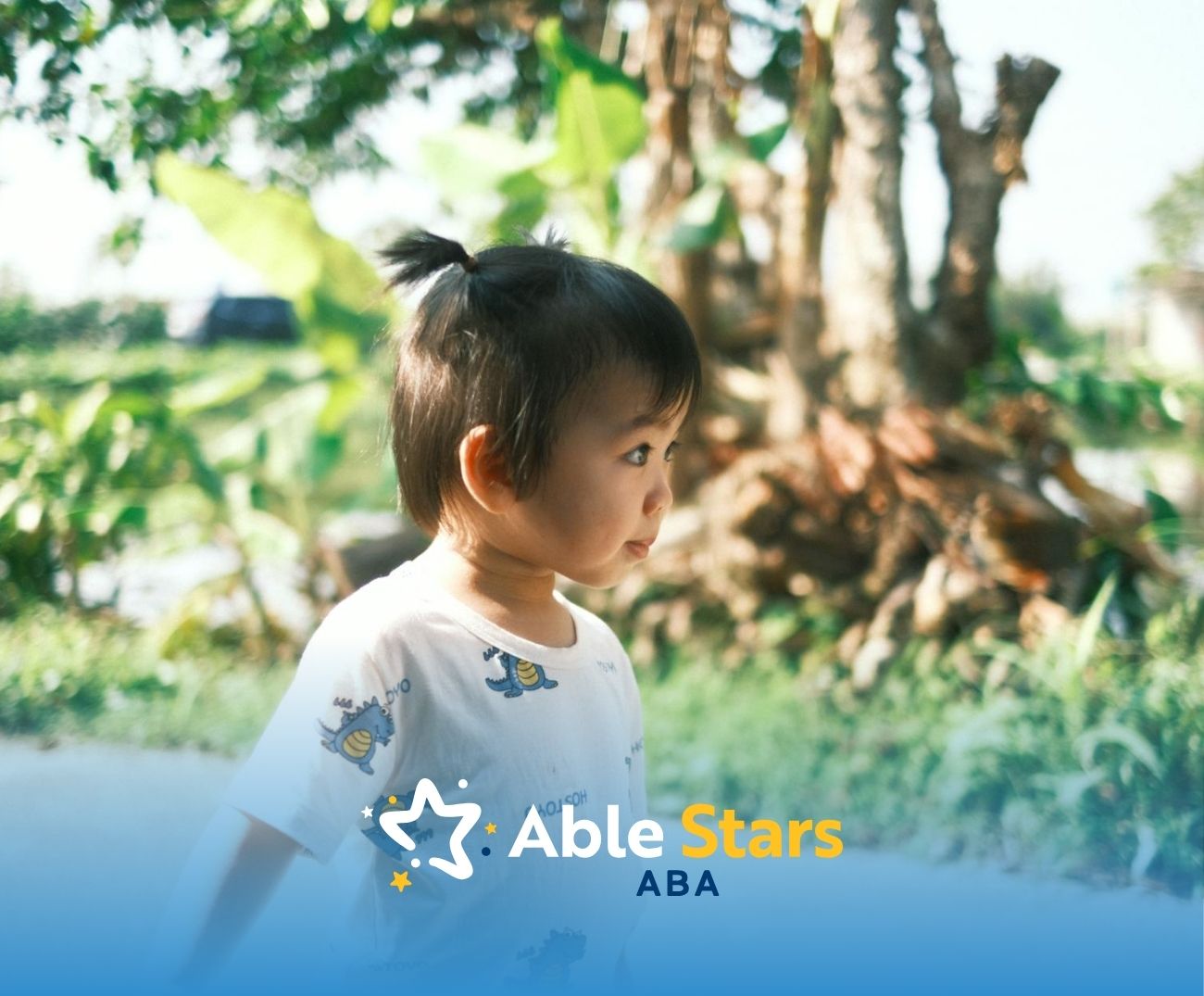 Autistic toddler with short ponytail standing outside in a sunny, green garden area in Maryland.