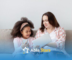 BCBA and autistic child smiling while looking at a tablet and phone.
