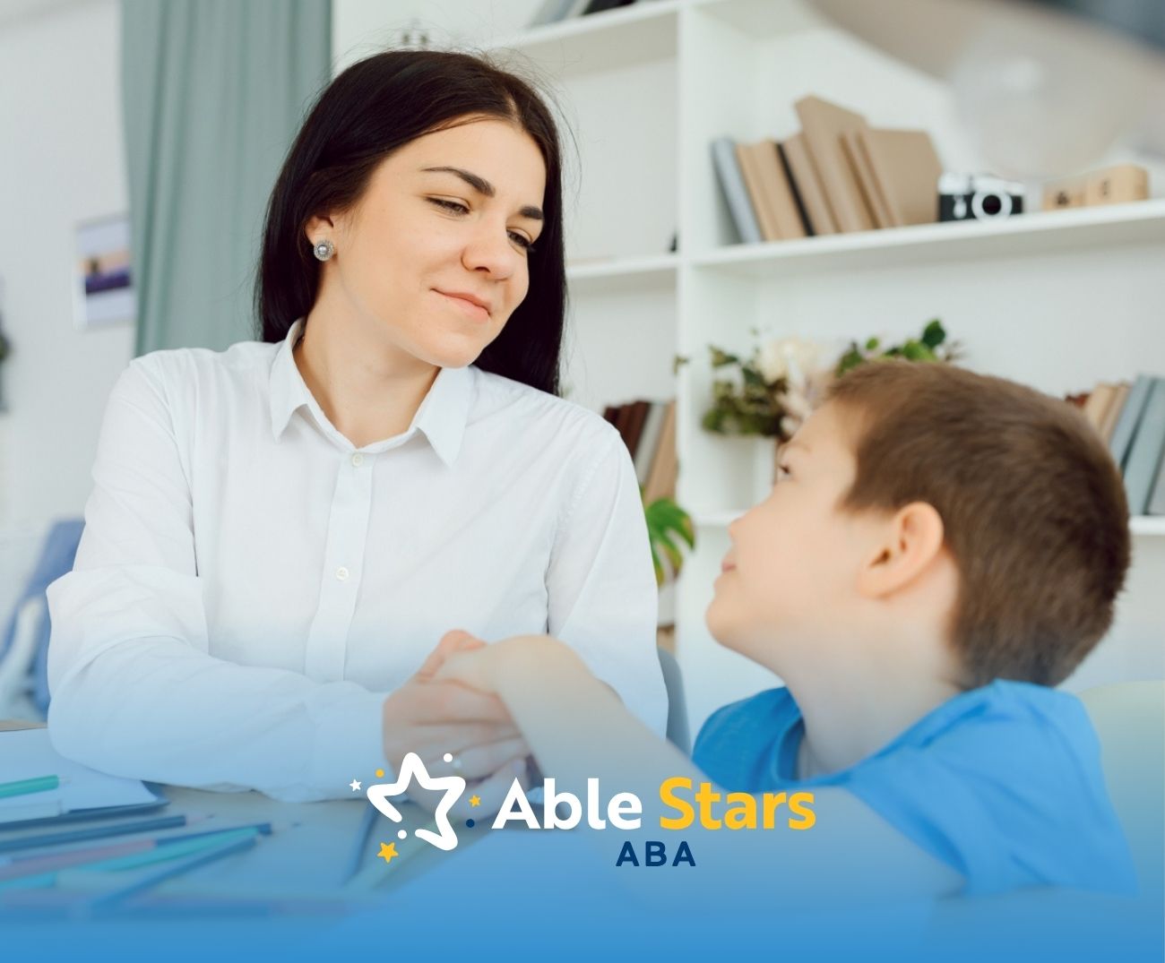 BCBA holding hands with a boy at a desk with colored pencils.