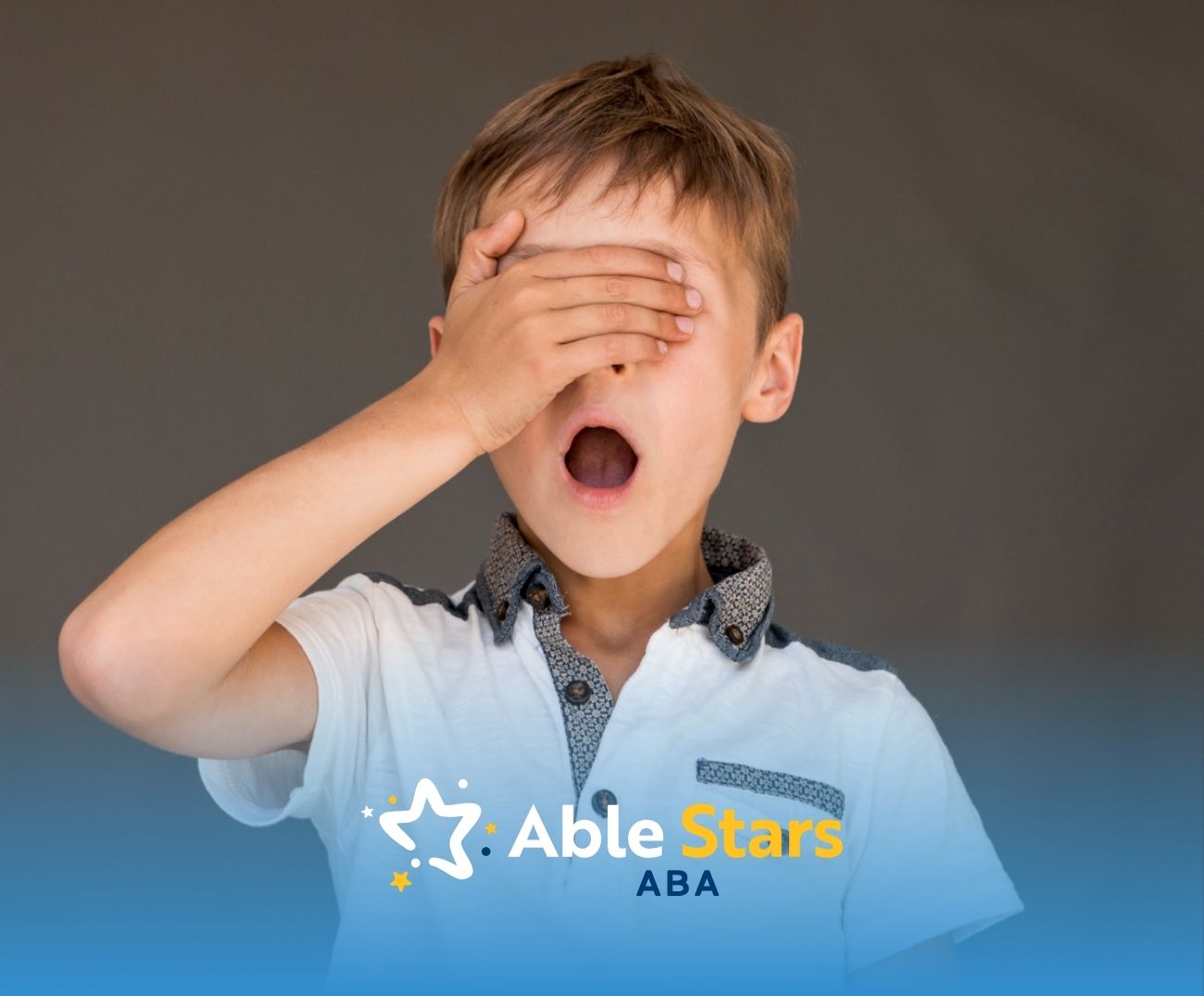 Autistic boy covering one eye with hand and yawning.