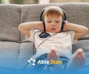 Young boy in a white T-shirt wearing headphones, relaxing on a gray sofa. He looks calm and immersed.