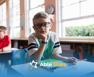 An autistic boy in glasses resting on hand at school desk with a workbook during school-based ABA therapy in MD.