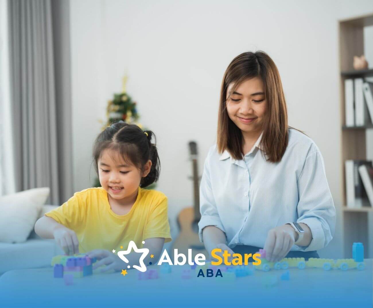 BCBA and young girl playing with colorful building blocks at a table indoors in ABA therapy.