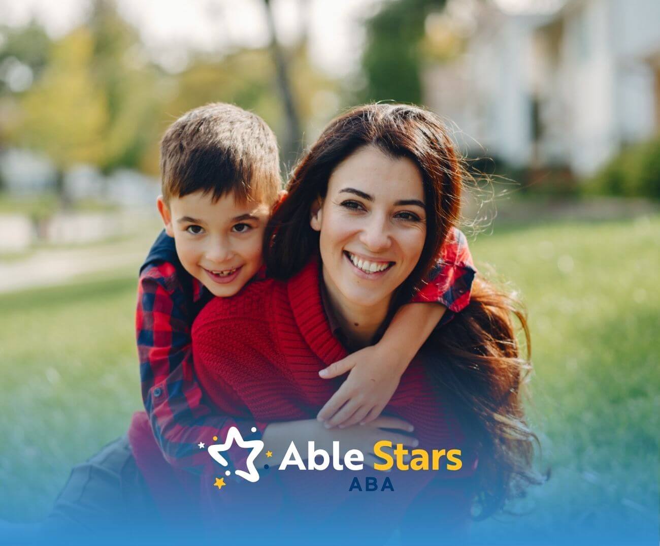 Smiling BCBA with young boy on her back, both wearing red, enjoying time outdoors during ABA therapy.