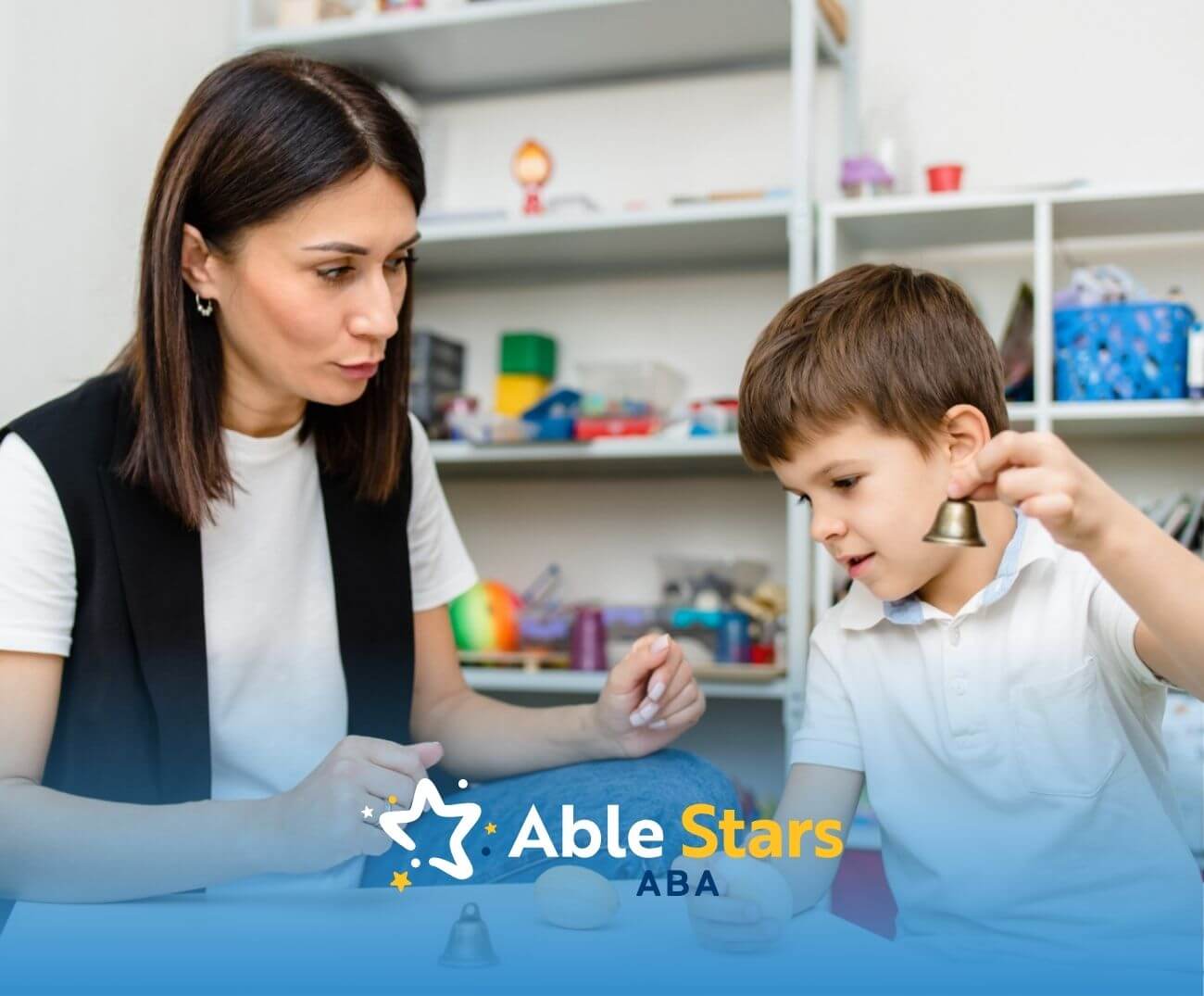 ABA therapist and boy interacting with small bells and wooden toys in ABA therapy.