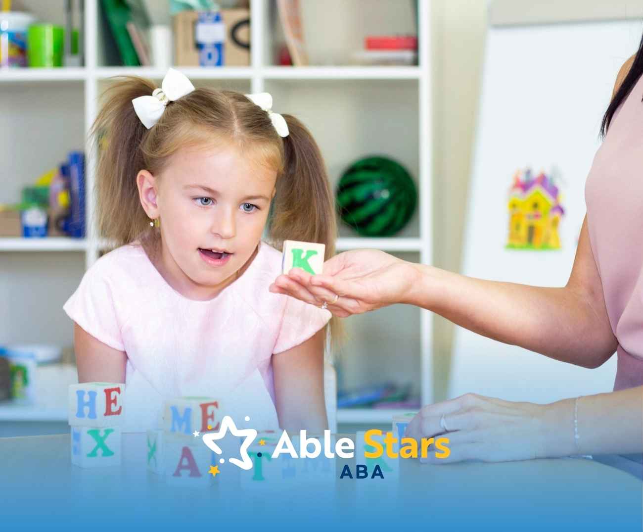 A young girl in pigtails eagerly examines a letter block handed by an adult. Colorful blocks and educational items fill the bright, inviting space.