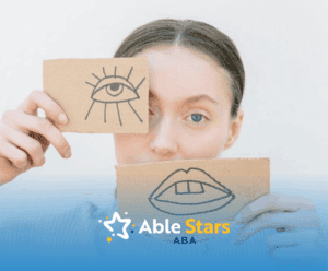 An autistic teen girl holding cardboard drawings of eye and lips during school-based ABA therapy in MD.
