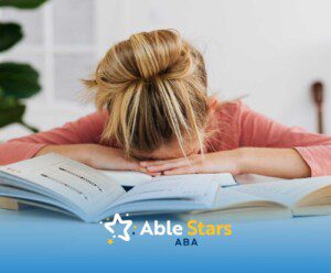 A child with blond hair rests their head on their arms atop an open book, appearing tired or frustrated.