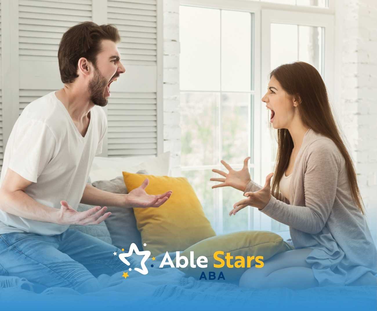 A man and woman sitting on a couch are yelling at each other in a brightly lit room, expressing anger.