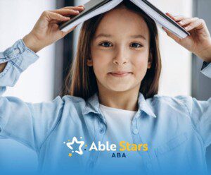 Smiling girl with autism holds book over head in ABA therapy.