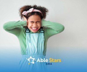 Child wearing a pink headband and pastel-colored overalls covers their ears with a distressed expression.