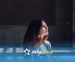 Young woman with autism sitting in sunlight, looking thoughtful indoors.