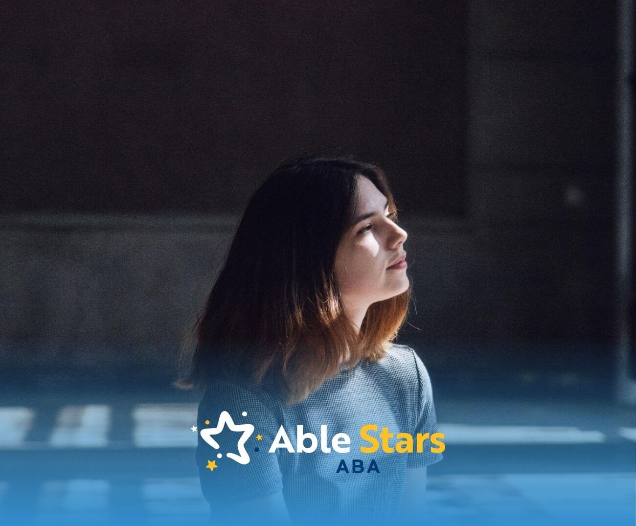 Young woman with autism sitting in sunlight, looking thoughtful indoors.
