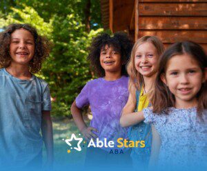 Group of four diverse children with autism smiling brightly outdoors against a wooden background.