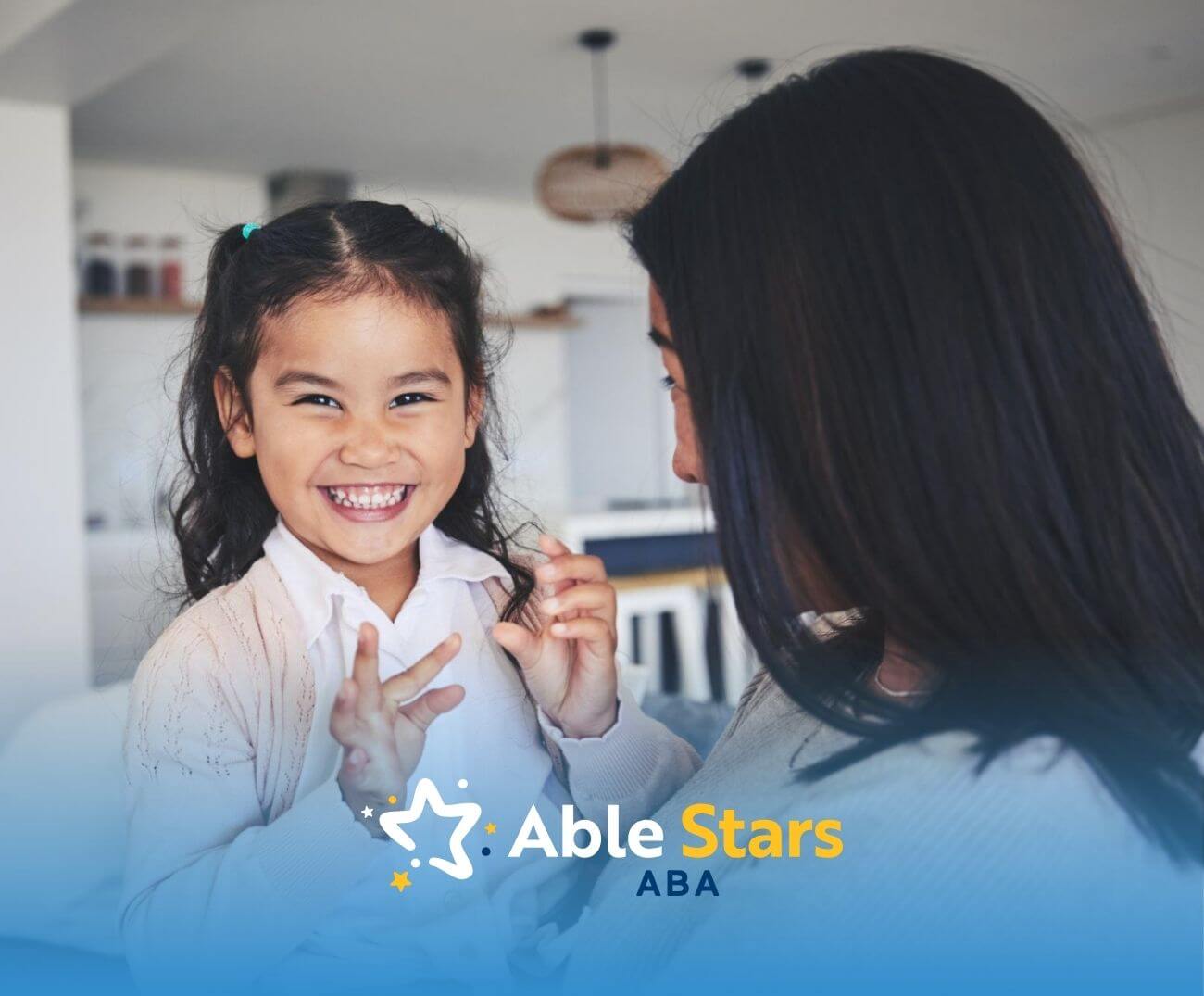 Young girl with autism smiling brightly while sitting on a BCBA's lap in a cozy home.