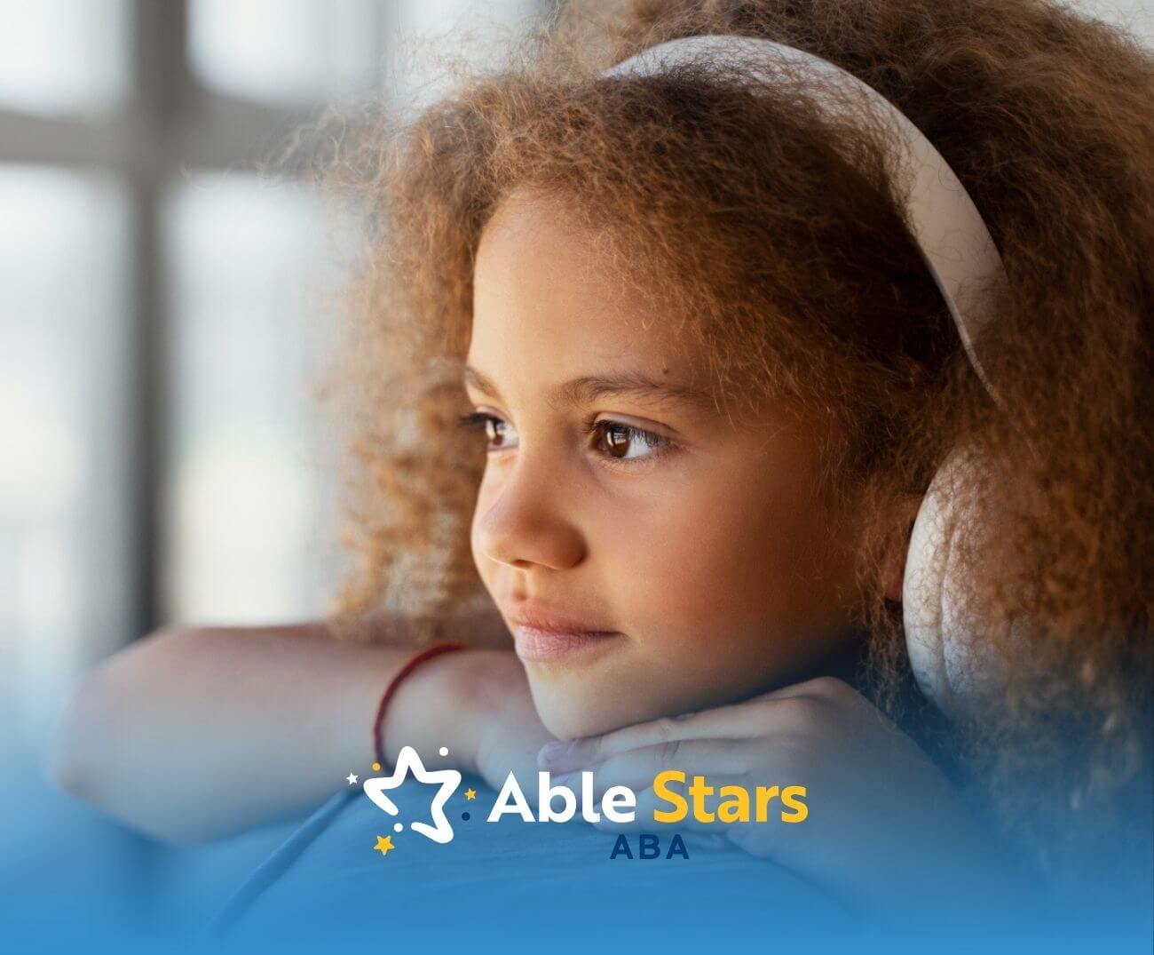 Young girl with curly hair wearing headphones and looking out a window after ABA therapy session.
