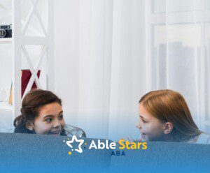 Two girls with autism laughing and peeking over the back of a couch while playing.