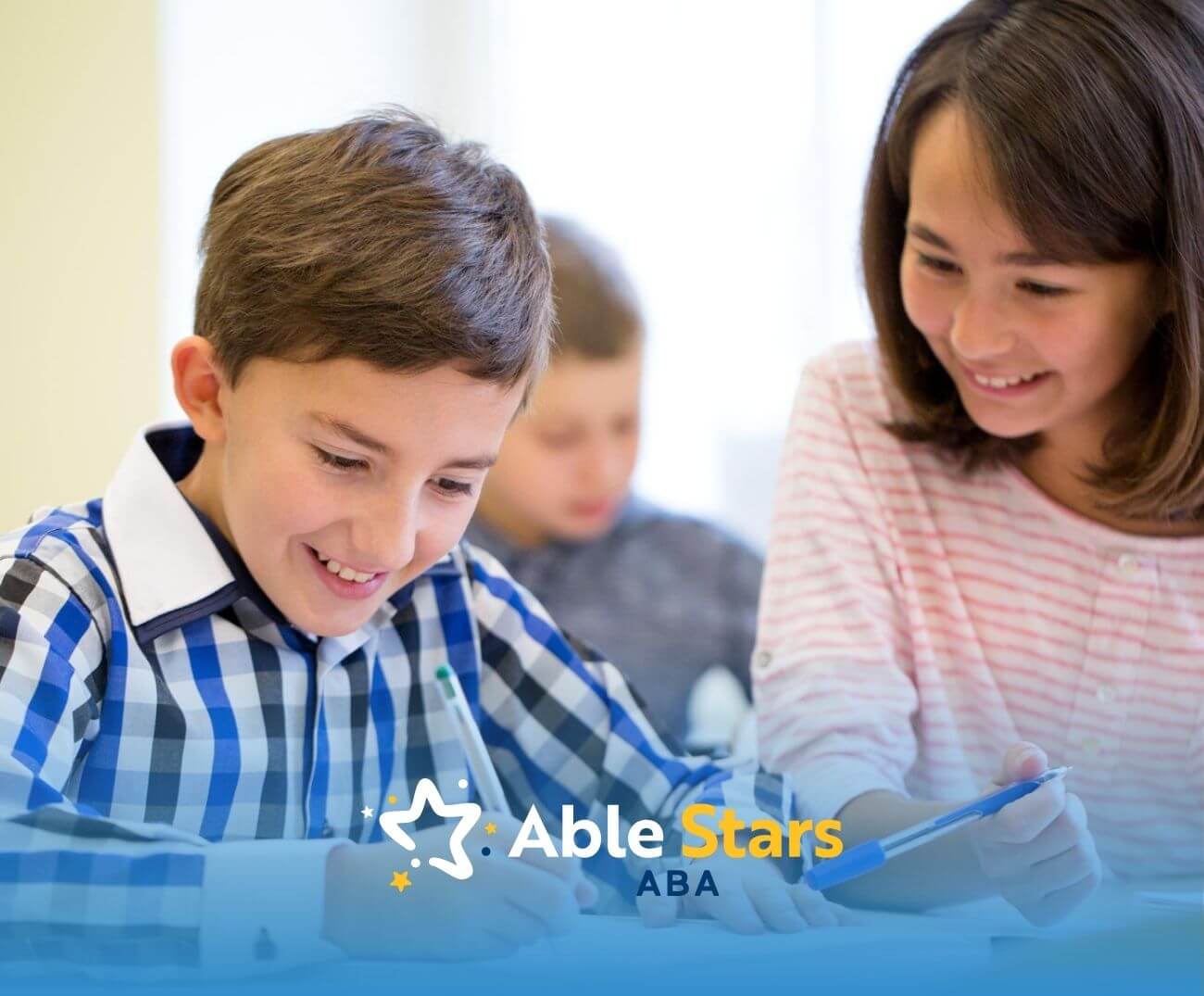 Two school-age kids with autism smiling while working together on homework at a desk.