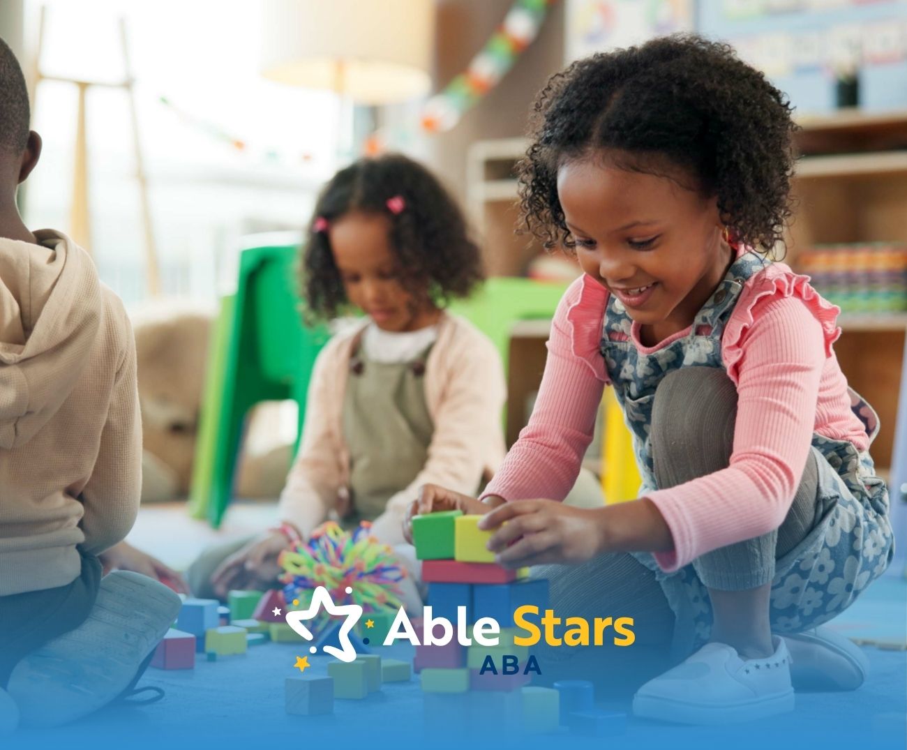 Children play with colorful blocks on a soft, blue mat in a cheerful classroom setting.