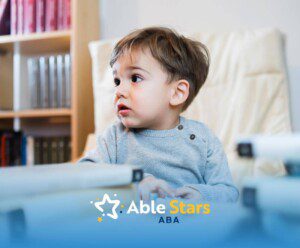 Young child with autism sitting in a chair surrounded by books, looking away with a curious expression.