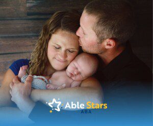 A loving family embraces a sleeping baby. The father kisses the mother's forehead, conveying warmth and tenderness.