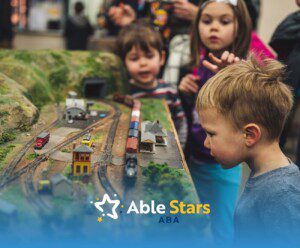Three children intently observe a model train on a detailed track layout.